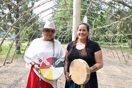Two First Nation women holding their indigenous drums in a non covered meeting hut