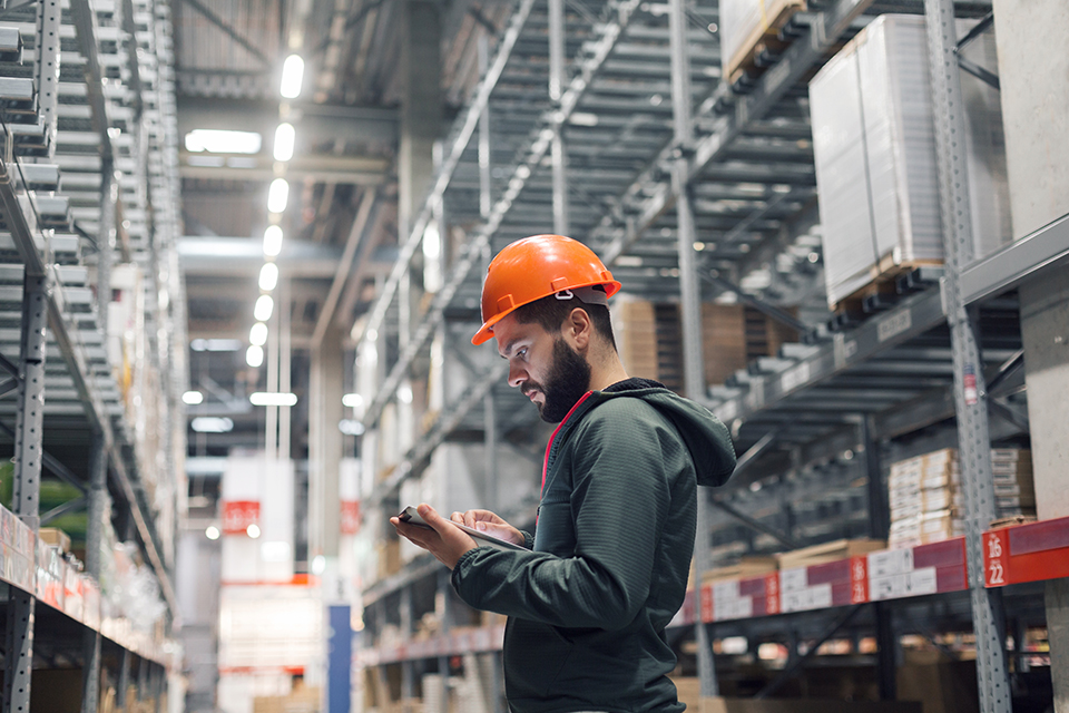 worker in warehouse with hardhat and using an electronic tablet