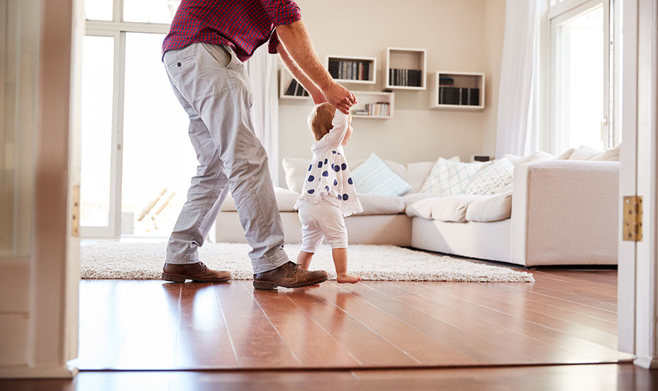 Parent assisting baby walk across living room